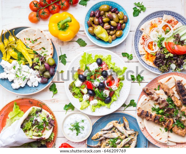 Greek food background. Meze, gyros, souvlaki,\
fish, pita, greek salad, tzatziki, assortment of feta, olives and\
vegetables. Traditional different greek dishes set. Top view. Food\
for share. Close-up
