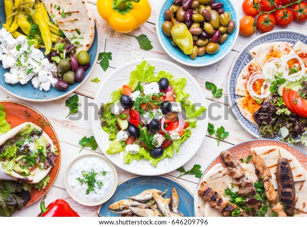 Greek food background. Meze, gyros, souvlaki,
fish, pita, greek salad, tzatziki, assortment of feta, olives and
vegetables. Traditional different greek dishes set. Top view. Food
for share. Close-up