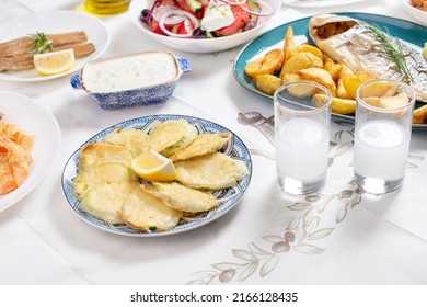 Greek Food Background. Ouzo, Zucchini, Greek Salad, Tzatziki, Assortment Of Feta. Roasted Dorado  Top View. Traditional Greek Taverna Menu. Close Up