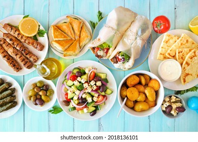 Greek Food Table Scene, Overhead View On A Blue Wood Background. Souvlaki, Gyros Wraps, Salad, Spanakopita, Pita And Tzatziki, Lemon Potatoes, Dolmades.