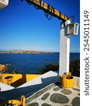 Greek idyllic romantic island feeling. whitewashed terrace steps. blue sky, Yellow wooden frame with a view of the sea and a small island in the distance. Vertical. Vravrona, Athens, Greece