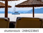 Greek island sailboat, Looking through beach umbrellas. Charter boat Island hopping with the blue Aegean waters. Luxury Holiday, sunset, vacation destination. 