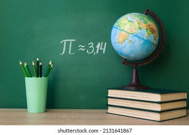 The Greek letter Pi is drawn in chalk on a green school blackboard with books, a globe, pencils in honor of the international day of March 14
