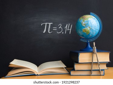 The Greek letter Pi the ratio of the circumference to its diameter, is drawn in chalk on a black school board with books, a globe and a compass in honor of the international number Pi for March 14