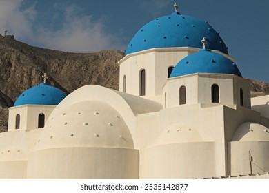 Greek Orthodox church in Perissa, Santorini, with distinctive white facade and blue domes. - Powered by Shutterstock