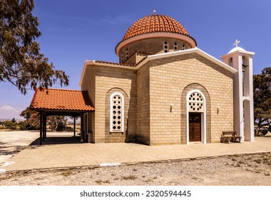 Greek Orthodox Church of Petounda is Made of Yellow Lime Brick with Round Windows, an Arched Entrance, High Bell Tower and Cross on Red Tiled Roof in Shade of Green Trees (Mazotos, Larnaca, Cyprus) - Powered by Shutterstock