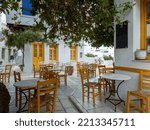 Greek outdoors tavern restaurant at Tinos island, Pyrgos village Cyclades Greece. Tables, straw chairs on cobblestone. Buildings background, plants.