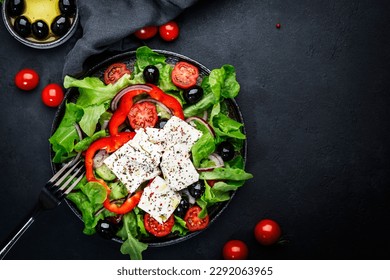 Greek salad with feta cheese, olives, cherry tomato, paprika, cucumber and red onion, healthy vegetarian mediterranean diet food, low calories eating. Black stone background, top view, copy space