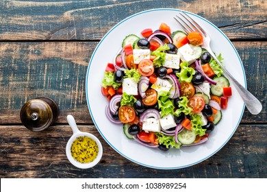 Greek salad of fresh cucumber, tomato, sweet pepper, lettuce, red onion, feta cheese and olives with olive oil. Healthy food, top view - Shutterstock ID 1038989254