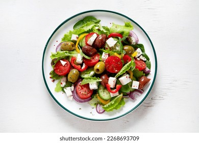 Greek salad of fresh cucumber, tomato, sweet pepper, lettuce, red onion, feta cheese and olives with olive oil on a white background. Healthy food, top view. 