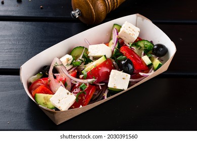 Greek Salad To Go In Paper Box, Greek Salad In A Takeaway Box On A Black Wooden Table. Takeaway Food.