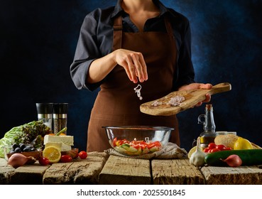 Greek Salad Making Process. The Chef Prepares A Salad In A Large Glass Bowl. Colorful Ingredients. Vegetarian And Sports Food, Healthy Food, Diet. Concept - Restaurant, Cafe, Fitness Bar.