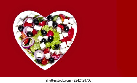 Greek salad in a plate in the shape of a heart on a red background. - Shutterstock ID 2242428705