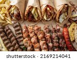 Greek street food variety, gyro sliced meat pita bread wrap, chiken and pork souvlaki skewer. Wooden table, top view