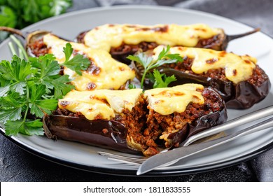 Greek stuffed eggplants with ground beef, tomatoes, topped with bechamel sauce with cheese, served on a plate with parsley on dark concrete background, top view, close-up