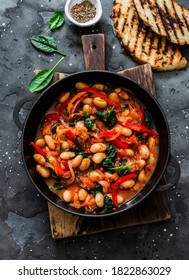 Greek style tomato sauce, spinach, paprika, beans stew in a cast iron pan on a rustic board on a dark background, top view. Simple comfort food                