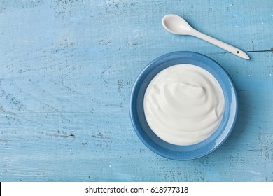 Greek yogurt in blue bowl on rustic wooden table top view.