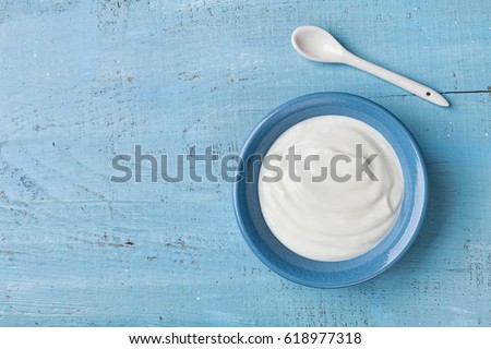 Greek yogurt in blue bowl on rustic wooden table top view.