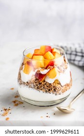 Greek Yogurt Granola Parfait With Peaches In Glass On White Marble Background. Healthy Snack, Breakfast Or After Workout Meal