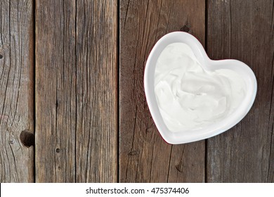 Greek yogurt in a heart shaped bowl, downward view over a rustic wood background