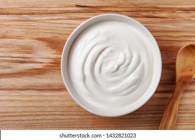 Greek Yogurt In White Bowl On Wooden Table Top View.