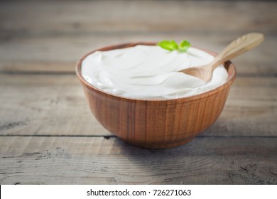 Greek yogurt in a wooden bowl on a rustic wooden table. Selective focus