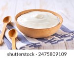 greek yogurt in a wooden bowl with spoon on a white table, selective focus.