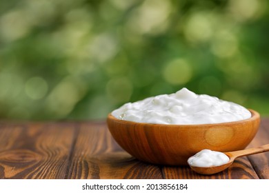 Greek Yogurt In Wooden Bowl With Spoon On Table Outdoors