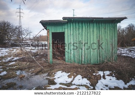 green abandoned wooden garden house in neglected territory, Latvia, late winter or early spring, snow melting, dry grass, dirty field