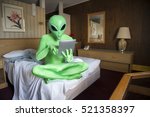Green alien sitting using tablet computer on the bed in an old-fashioned room