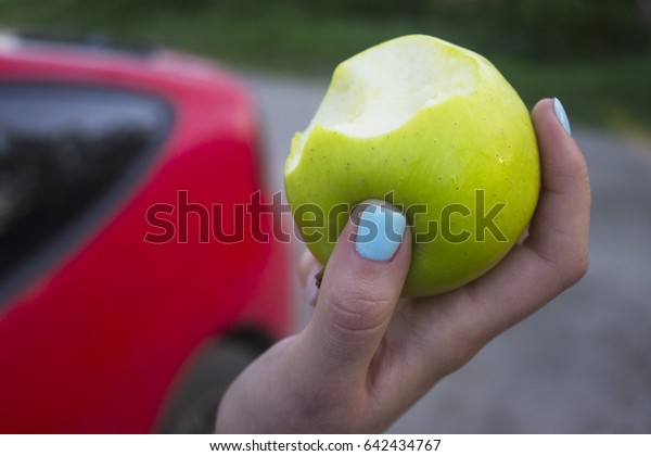 Green\
apple was bitten on the background of a red\
car