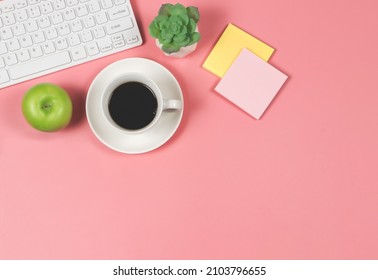 Green apple with black coffee cup, computer keyboard, succulent plant pot and sticky note paper. on pink background with copy space.  Healthy snack and lunch with working in office. Healthy Lifestyle 
