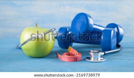 Green apple, measuring tape, dumbbells, stethoscope on the blue background.