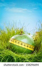 Green Apple And Measuring Tape On The Green Grass.