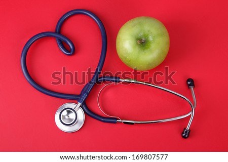 Green apple and stethoscope isolated on red background