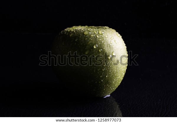 Green apple with a touch of\
water sprinkled on it and a small shadow of light to light up the\
object