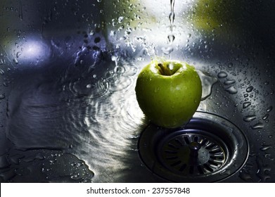 Green apple under the pressure of water in the kitchen sink