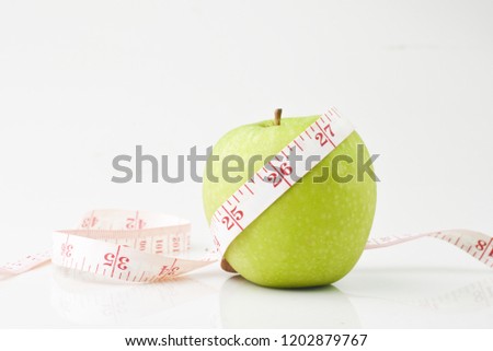 Green apple wrapped by measuring tape with 25,26 and 27 scale and white isolated background. Weight loss with fruit diet conceptual. Selescted focus.
