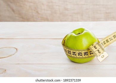 Green apple wrapped with a centimeter tape on a wooden desk