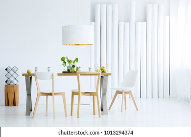 Green apples placed in metal basket standing on oak table in white dining room interior with plant
