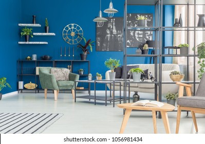 Green Armchair Against Navy Blue Wall In Living Room Interior With Black Posters And Gold Clock