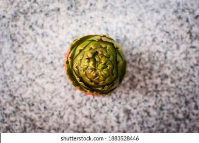 Green Artichoke In A Wooden Bowl Over A Granite Countertop. Top Down View.