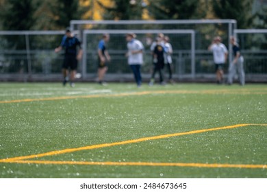 Green artificial turf football field with blurred athletes training in background, Football players training on green artificial turf field - Powered by Shutterstock