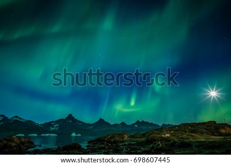 Green aurora and star burst moon over water and mountains in Greenland 