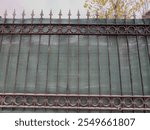 Green awning. A green mesh canopy extends along the iron railings. Added green mesh shadow for streetside path. Green garden fence. Plastic mesh acts as sun barrier, mesh textile, synthetic fibers. 