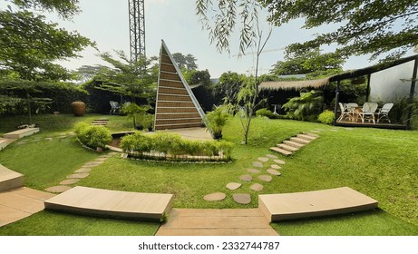 A green backyard with seating, water feature, triangular gazebo as center stage, and a tropical southeast asian clay urn or jar as focal point with shaded gazebo and rattan chairs at the background