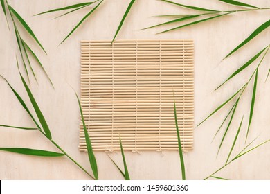 Green bamboo leaves and bamboo mat, asian style background, top view, copy space. Trendy bamboo leaves flat lay on white wooden background.