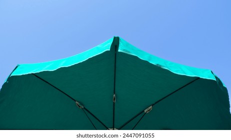 Green beach umbrella. Blue sky in the background. View from below. Relaxing context. Summer holidays by the sea. General contest and location - Powered by Shutterstock