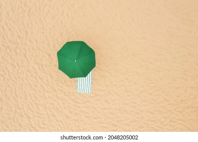 Green Beach Umbrella And Towel On Sandy Coast, Aerial View. Space For Text