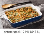 Green bean casserole with cheesy mushroom sauce and topped with crispy onions close-up in a baking dish on the table. horizontal
